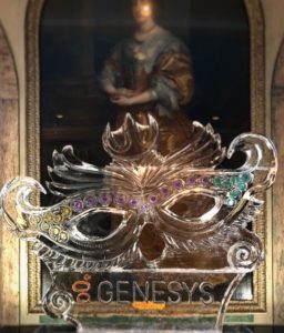 a Mardi Gras mask ice sculpture with a Gensys logo at the bottom. Displayed in front of a large painting at the Windsor Court Hotel.