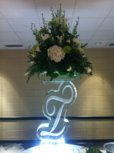 a script T ice stand with a large flower arrangement on top. By ice dragon ice sculptures